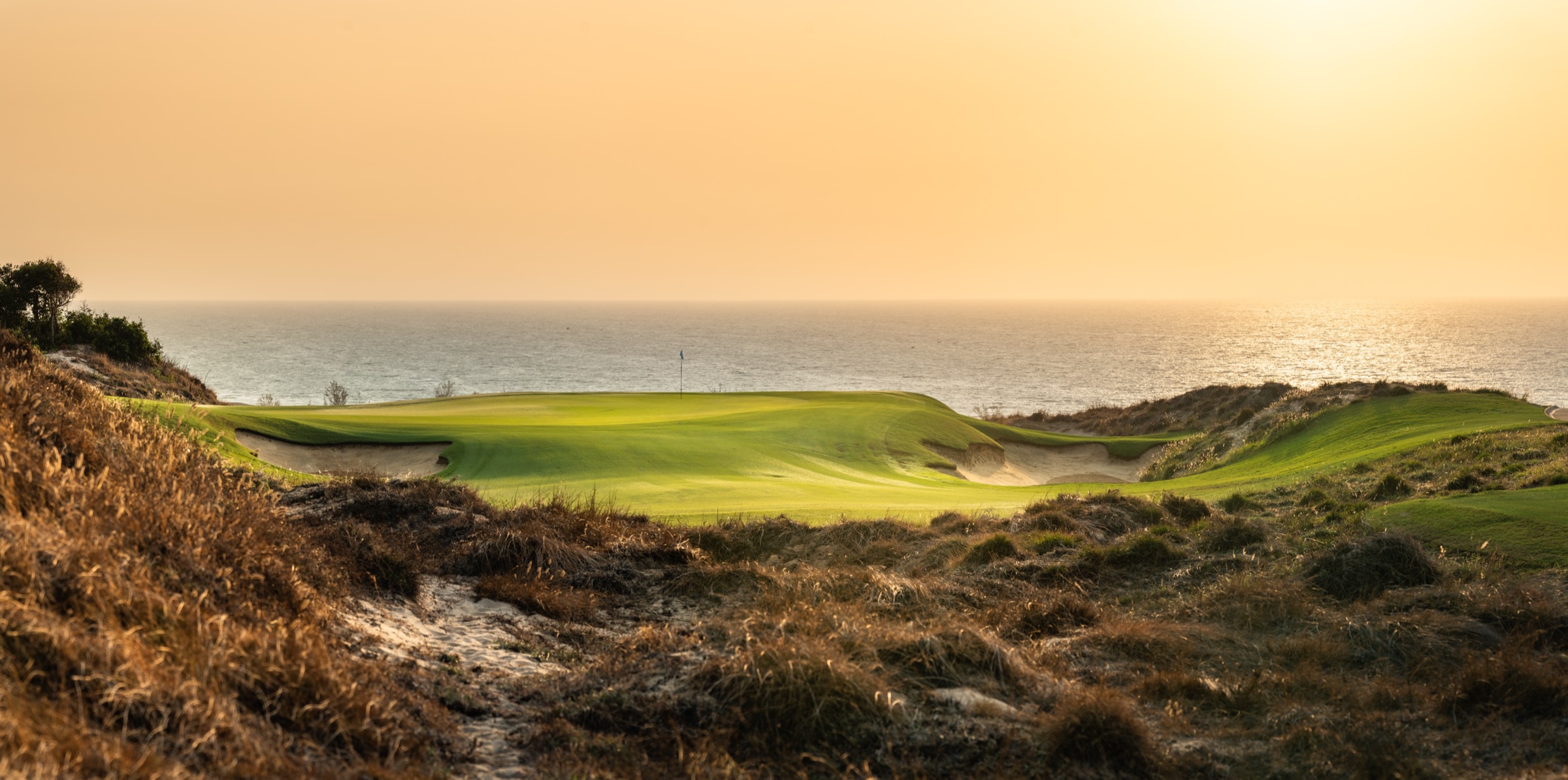 The Bluffs, Grand Ho Tram — coastal links green above the ocean at golden hour, Vietnam